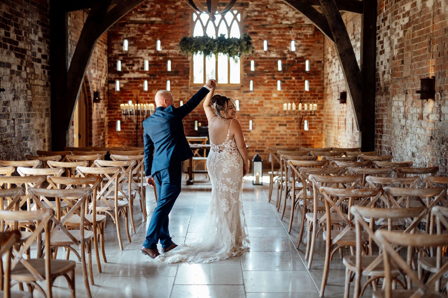 Rustic brick barn venue with wooden cross-back chairs set up for a wedding ceremony.