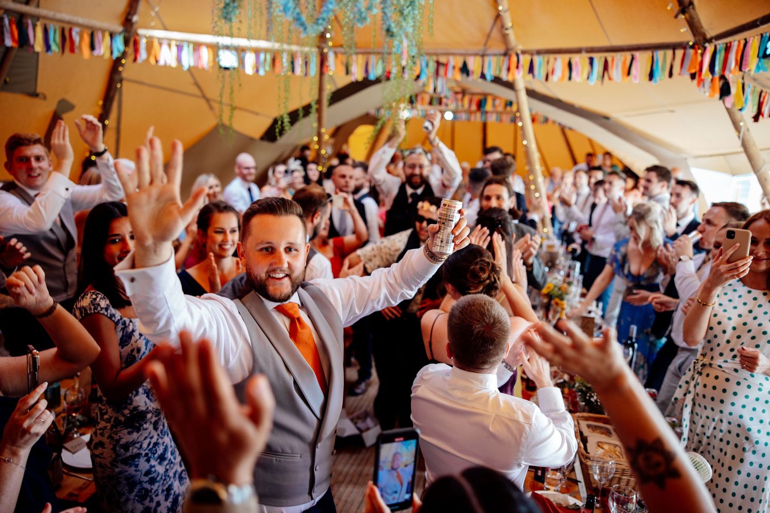 Enthusiastic wedding celebration with guests dancing under a decorated tent.