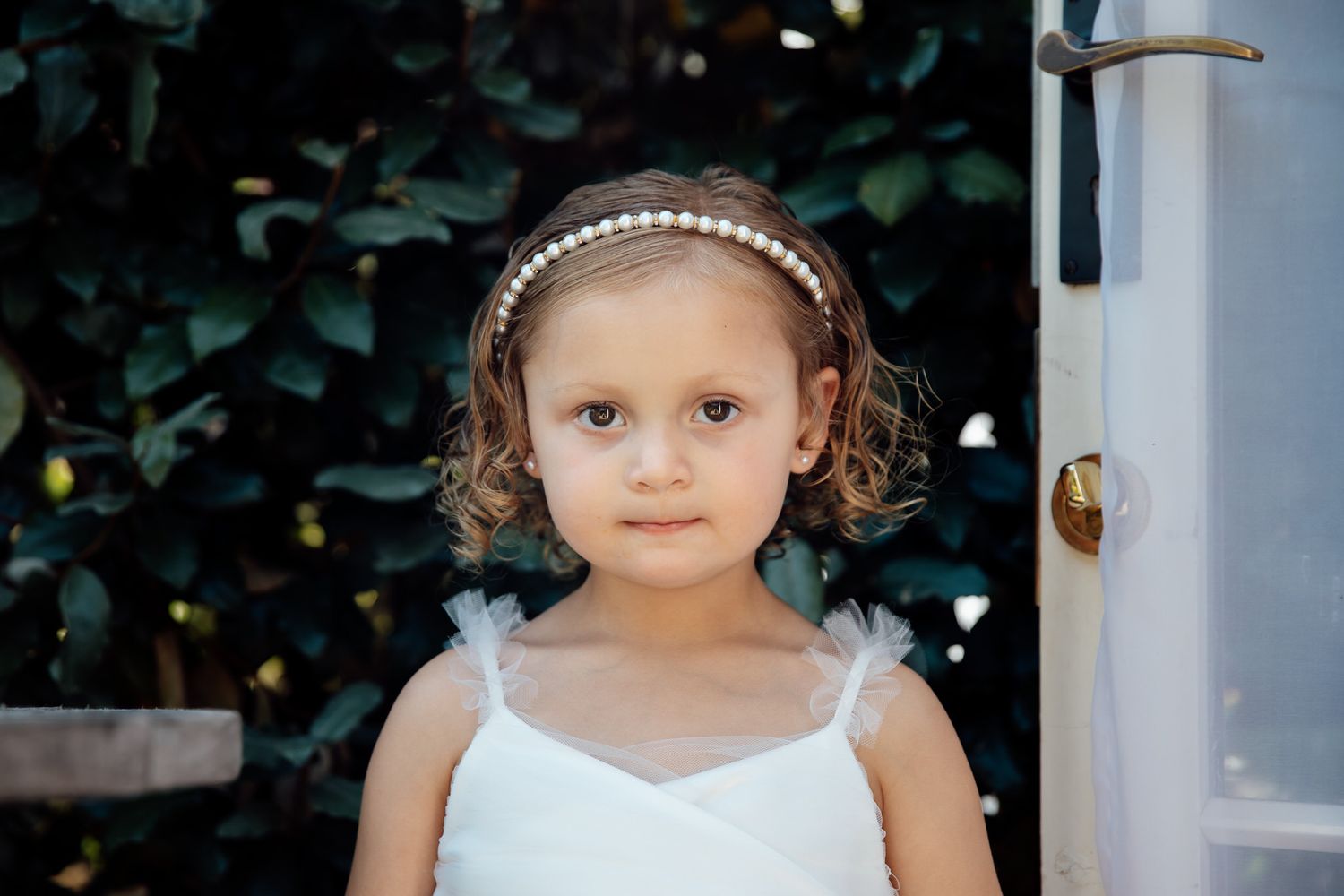 Small child wearing white dress and pearl headband.