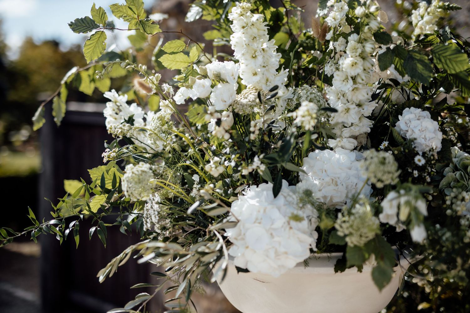 Elegant white floral arrangement with roses and greenery in natural outdoor lighting.