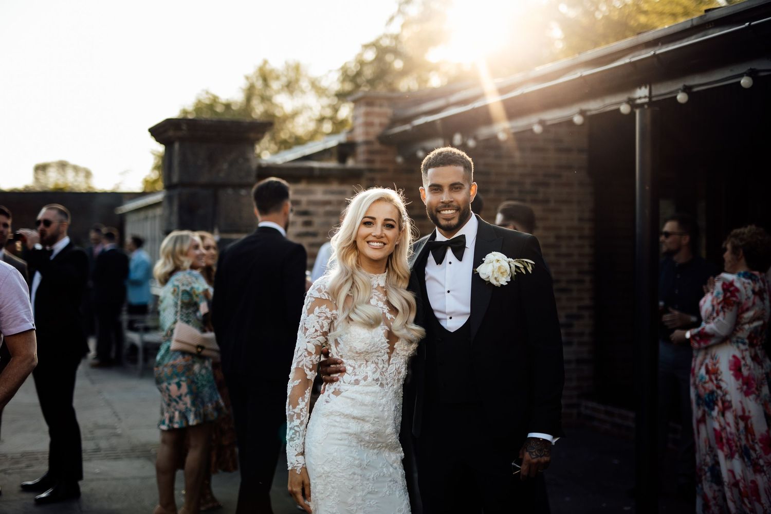 Wedding couple and guests celebrating during golden hour outside a brick venue.