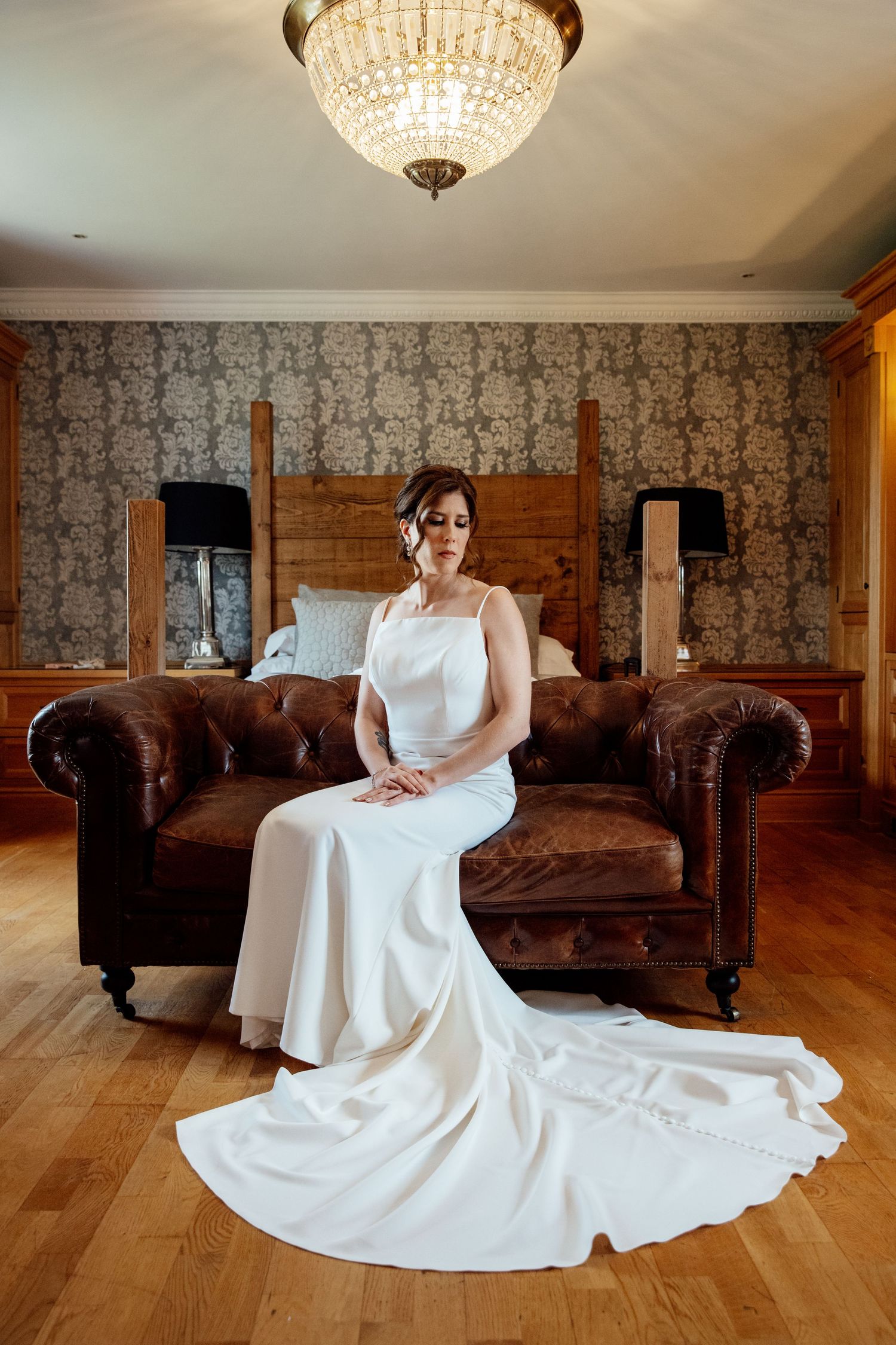 White wedding dress spread out on hardwood floor under crystal chandelier.