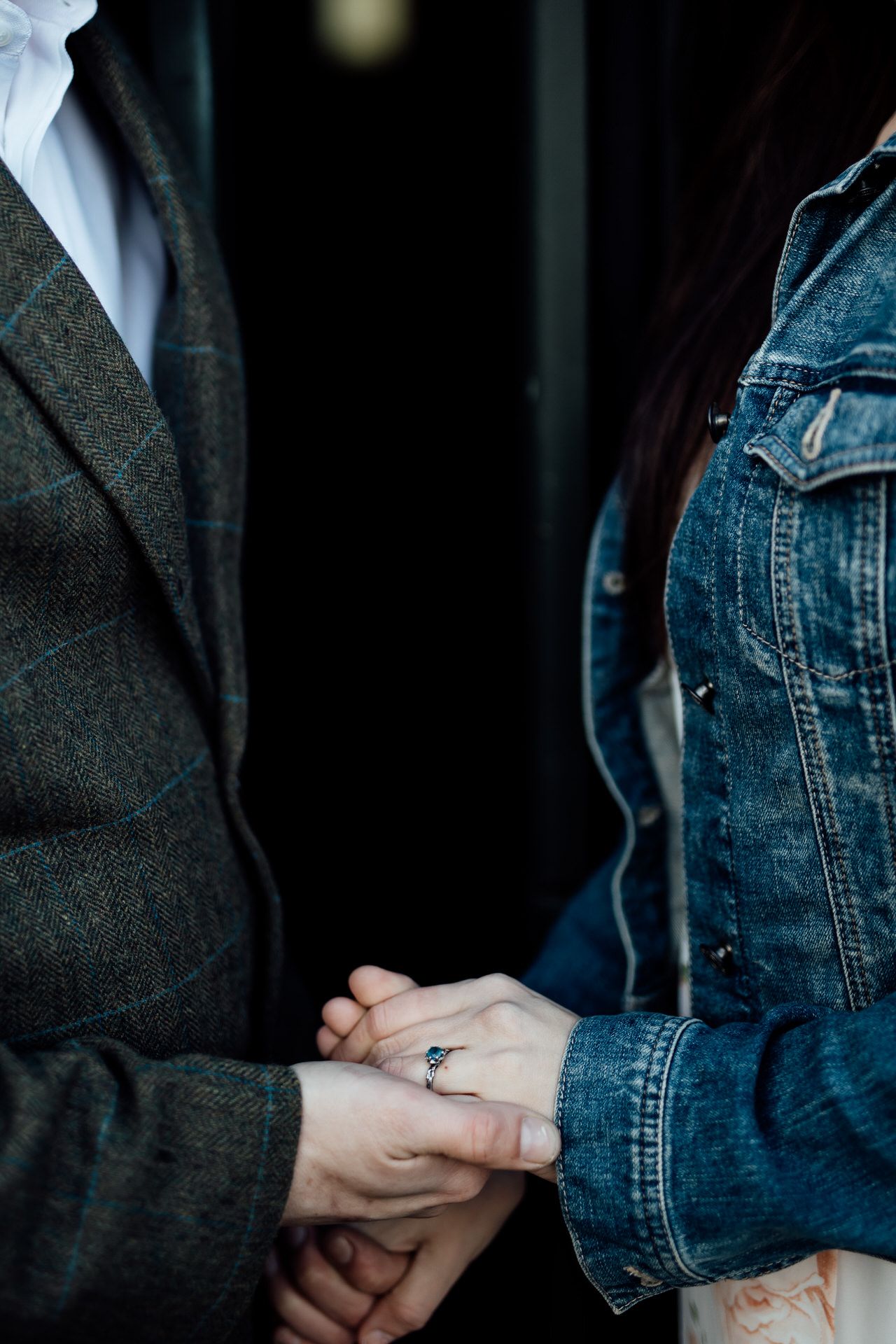 Close-up detail of hands tenderly holding each other, one wearing denim and the other a dark jacket.