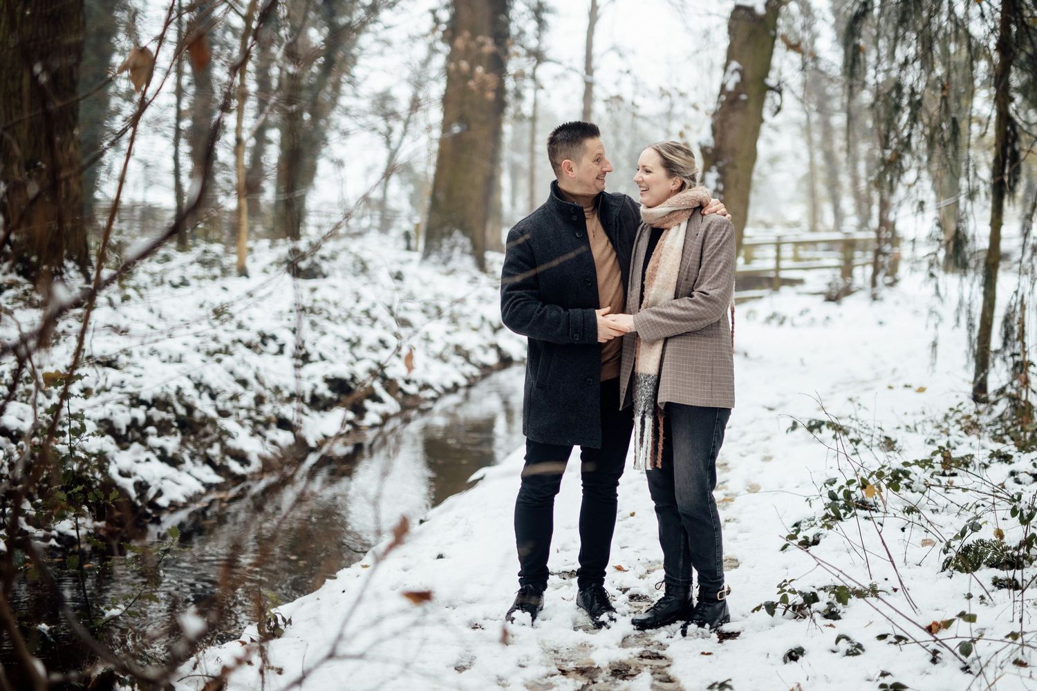 A couple takes a romantic stroll through a snow-covered forest path on a winter day.
