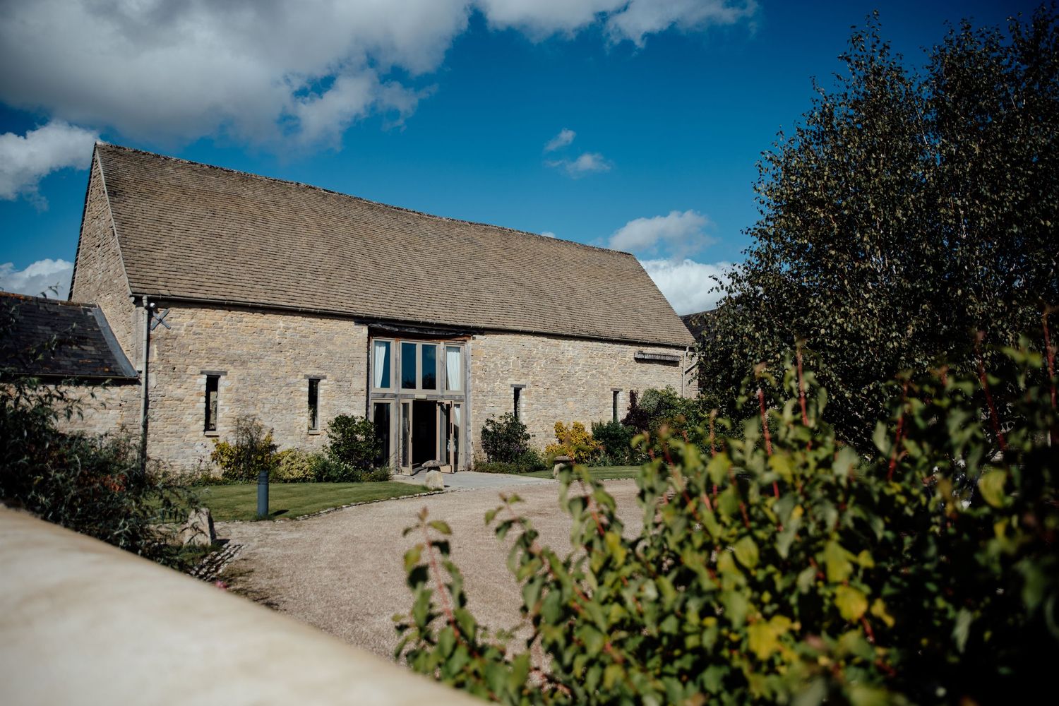 Stone barn wedding venue exterior with blue sky and white clouds.