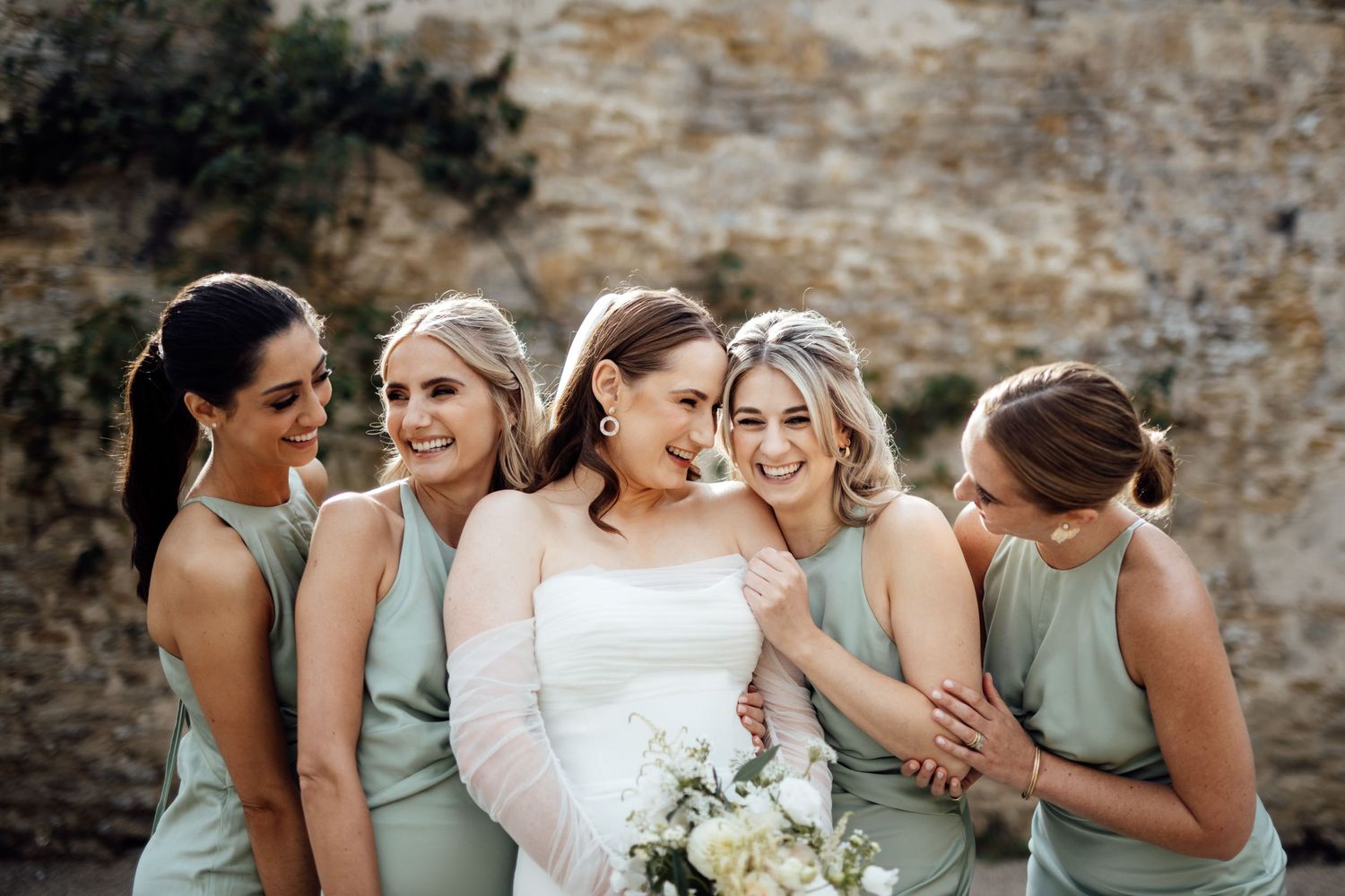 Wedding party in sage green dresses sharing joyful moment outdoors.