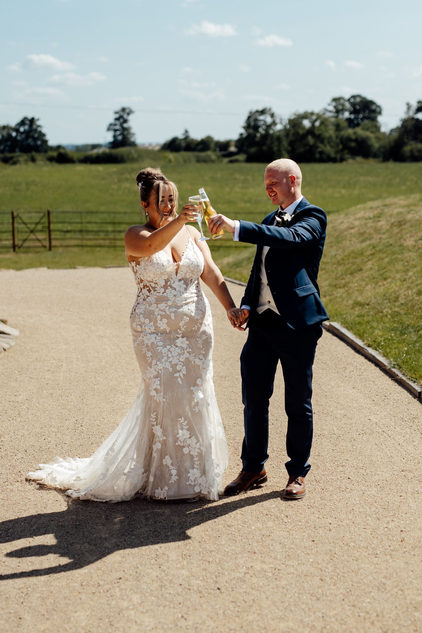 Newlyweds pose playfully on outdoor path surrounded by green countryside.