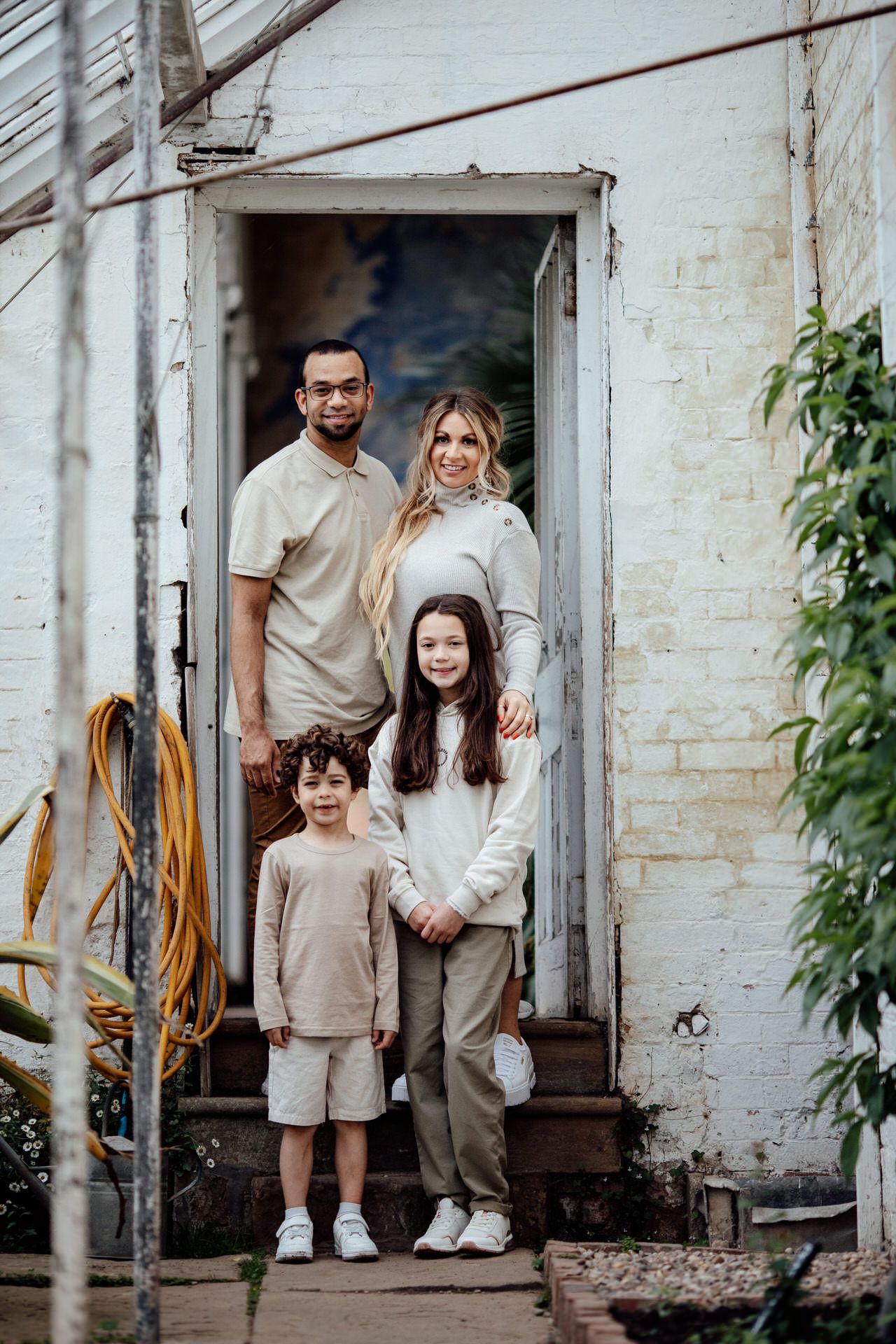A family poses together in coordinated beige and white outfits against a white brick wall.