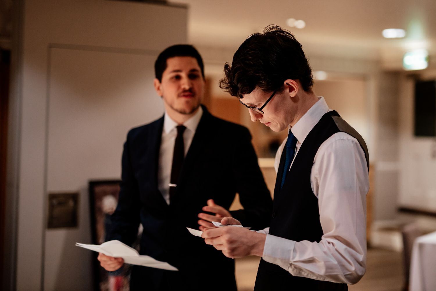 Wedding party members in formal attire review documents during an indoor reception.