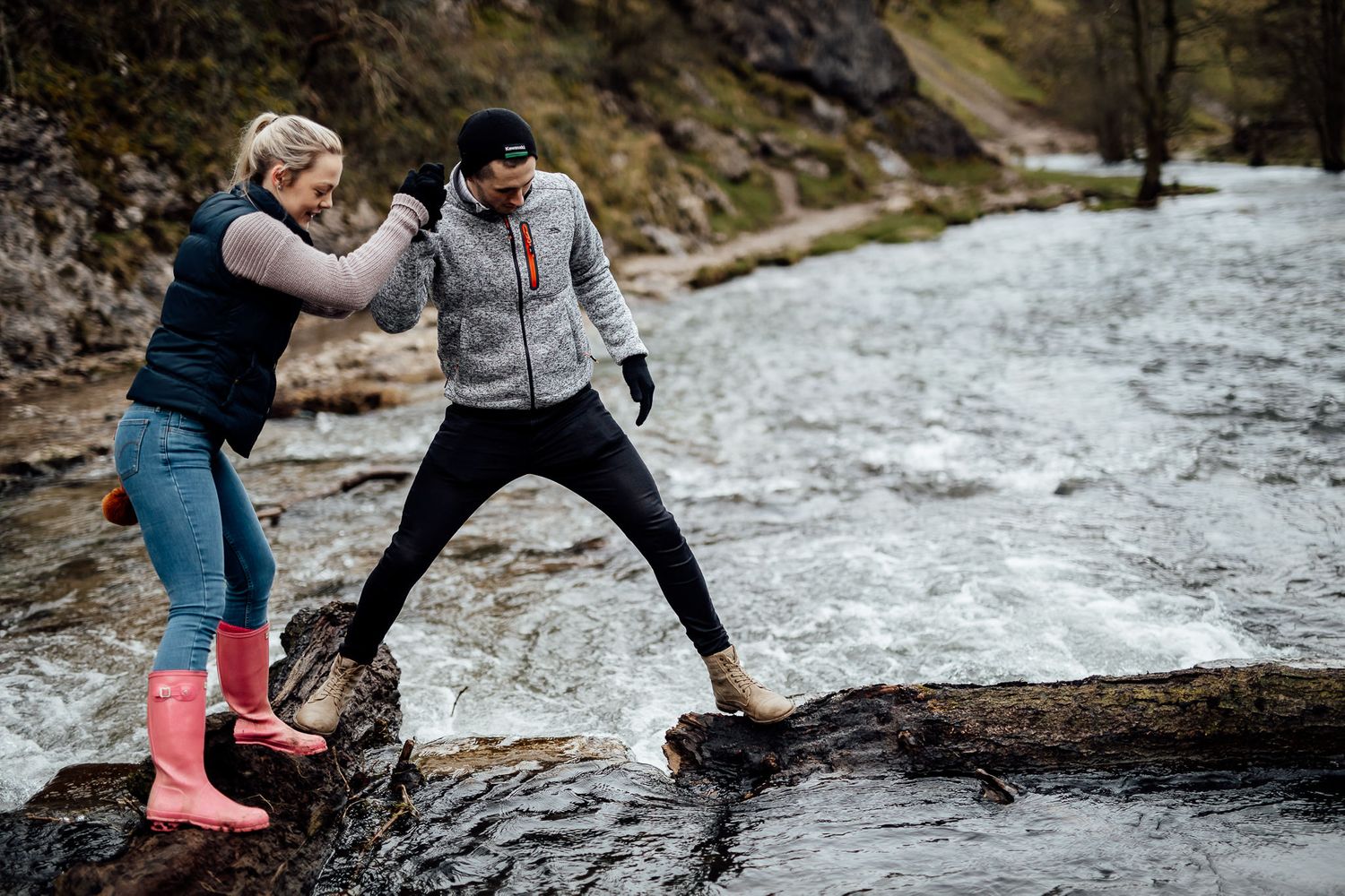 Two people share an intimate moment on rocky terrain near a stream.