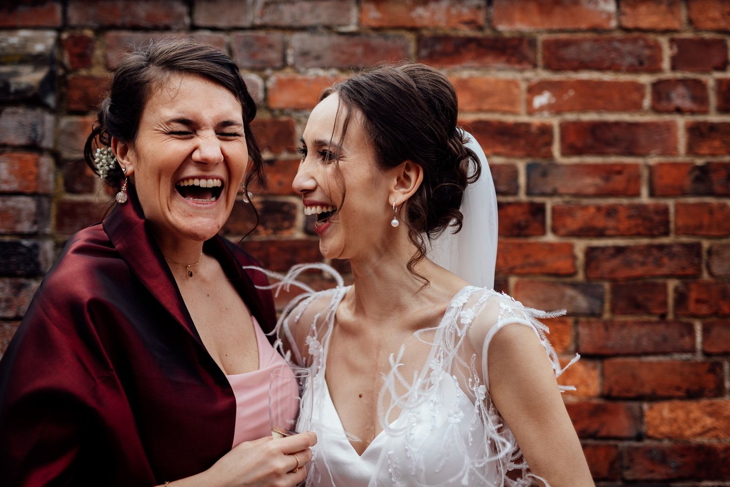Two people laughing together against a rustic brick wall background.