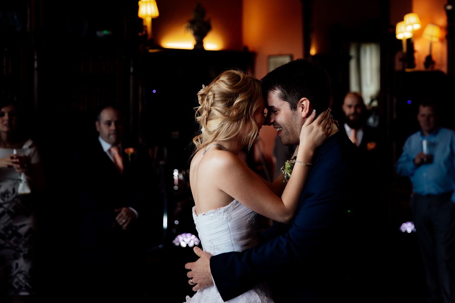 Couples dancing at dimly lit wedding reception with warm ambient lighting.