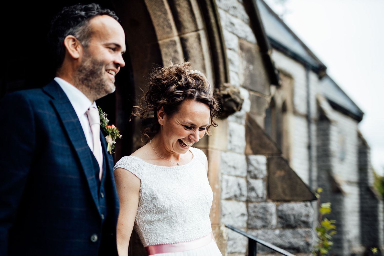 A couple poses together against a stone building exterior on their wedding day.