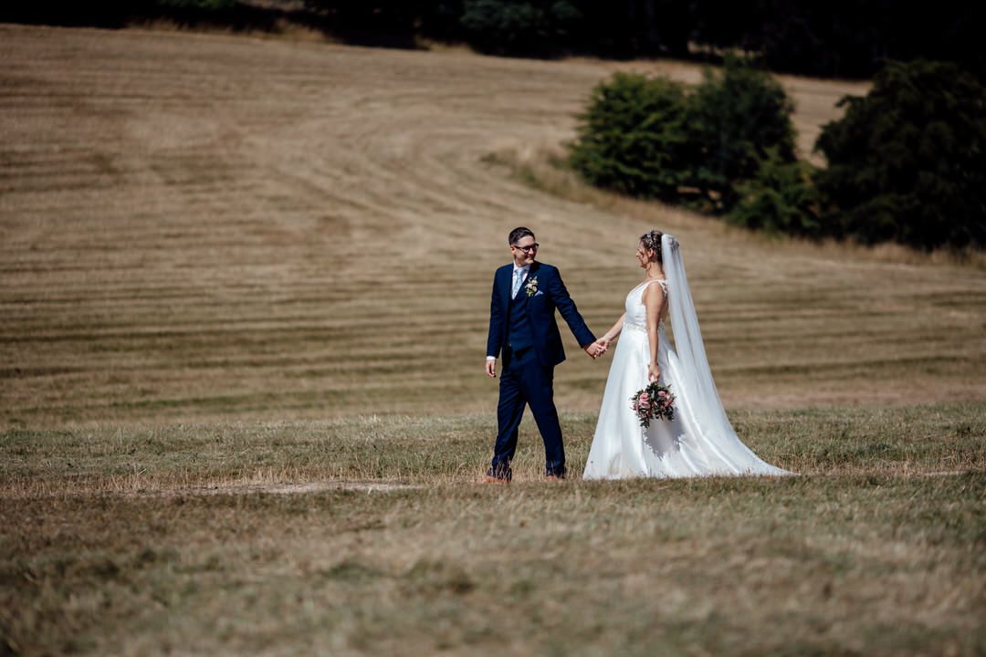 A couple poses for wedding photos in a rustic field during golden hour.