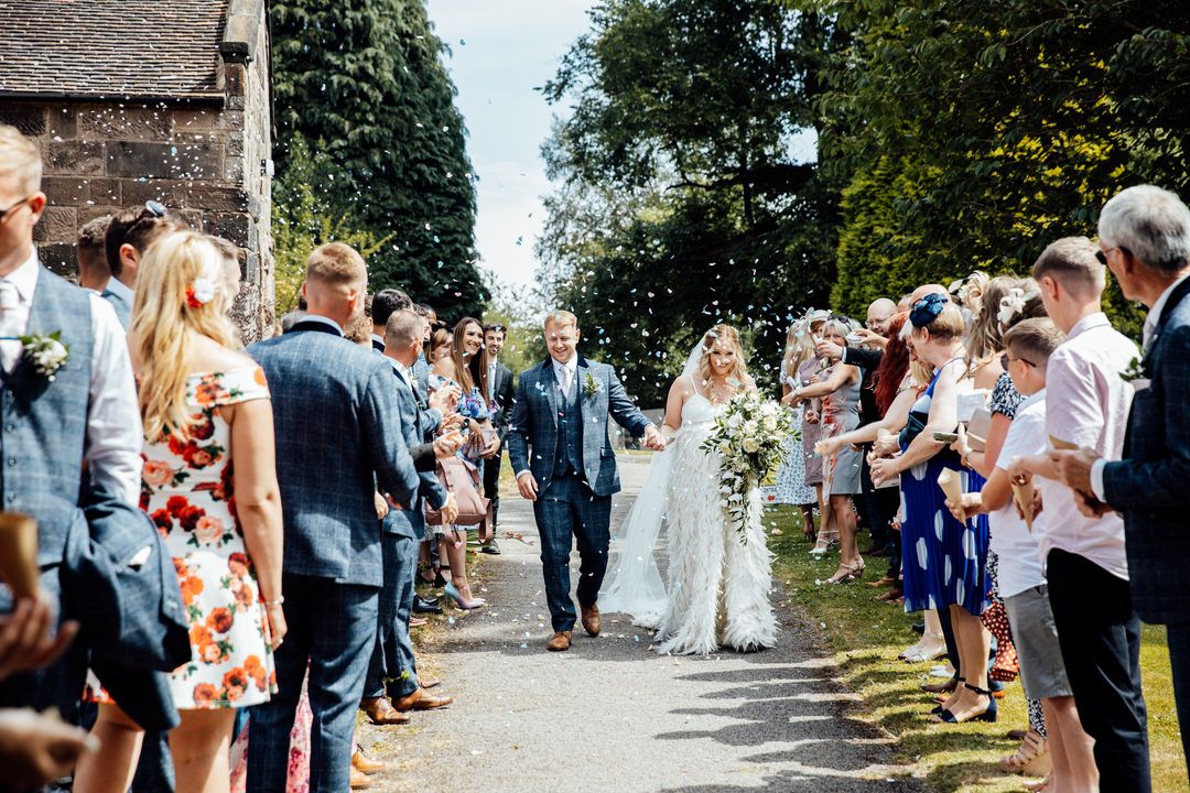 Wedding guests line a pathway throwing confetti at a countryside celebration.