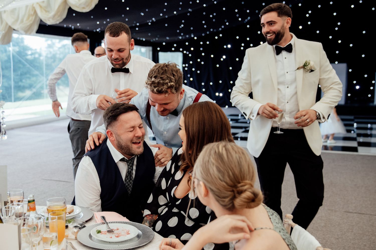 Wedding reception guests celebrate under twinkling lights at elegant venue.