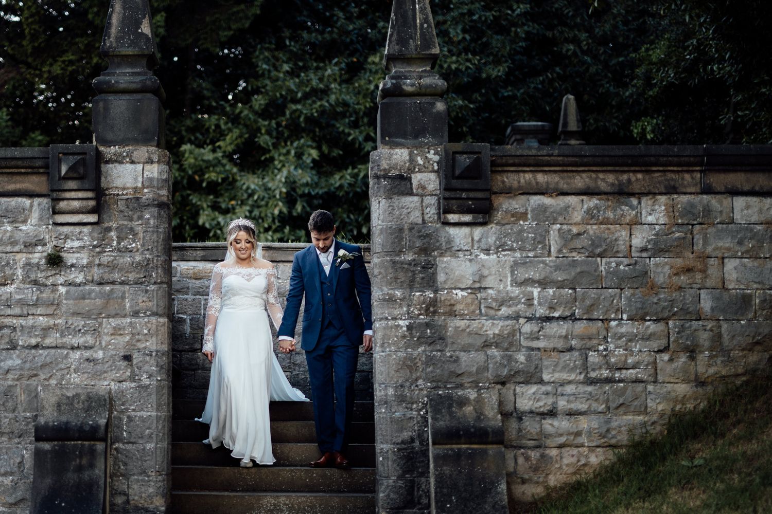 Wedding couple poses along historic stone wall for romantic portraits.