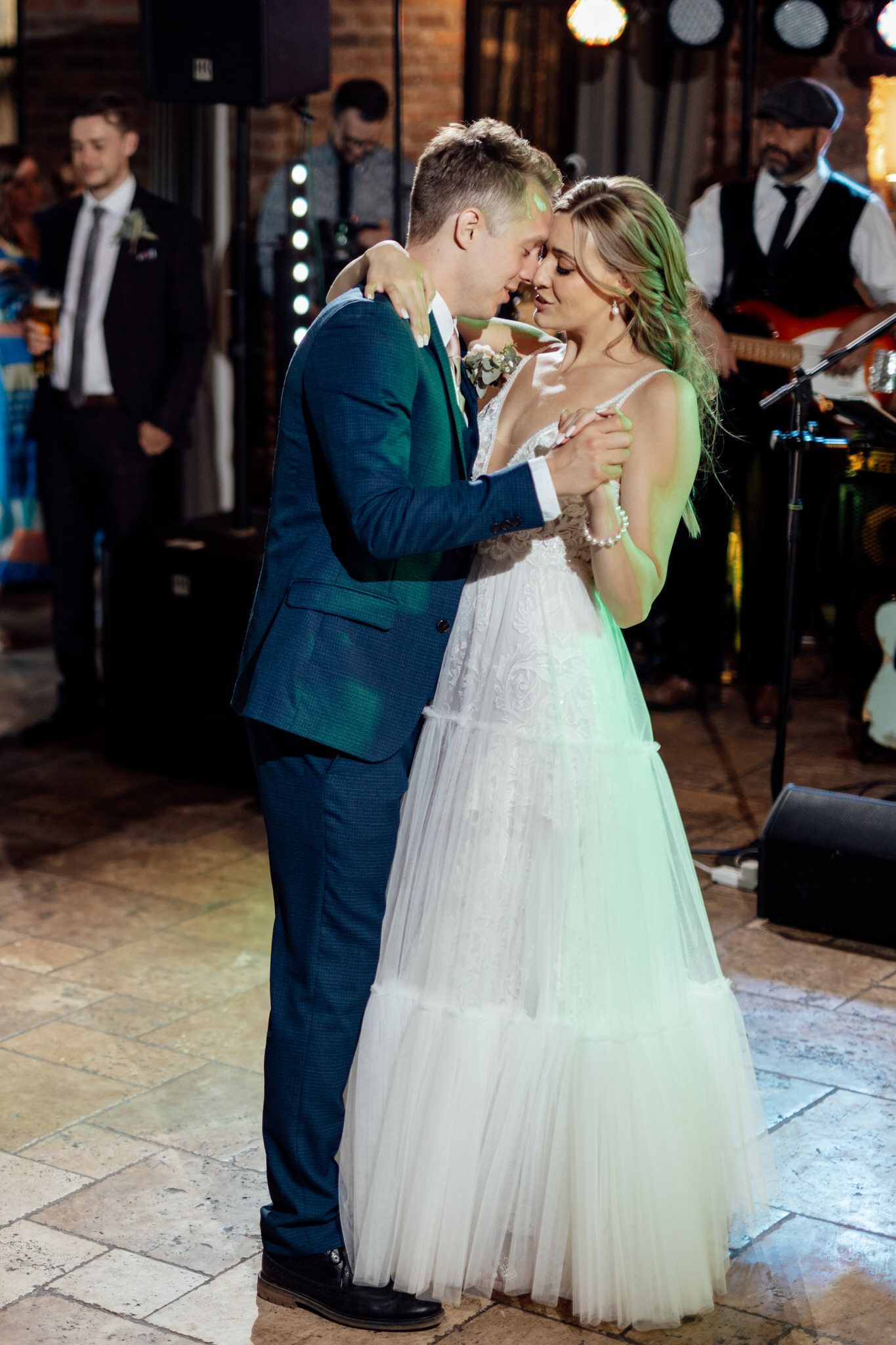 Newlyweds share their first dance on a stone floor under romantic lighting.