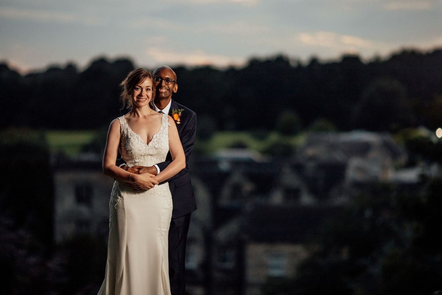 Newlyweds embrace during sunset with a scenic landscape view in the background.