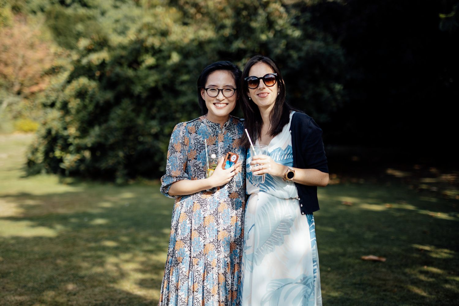 Two friends enjoying drinks together in sunny garden setting.