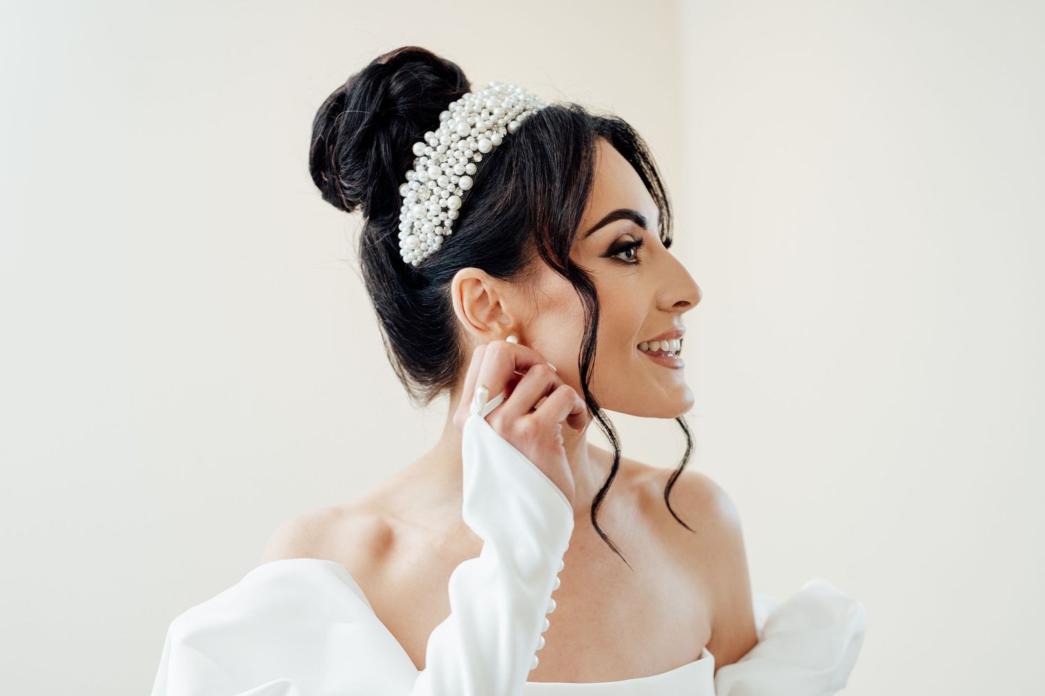 Elegant bridal portrait showing off a pearl headpiece, updo hairstyle and off-shoulder wedding dress.