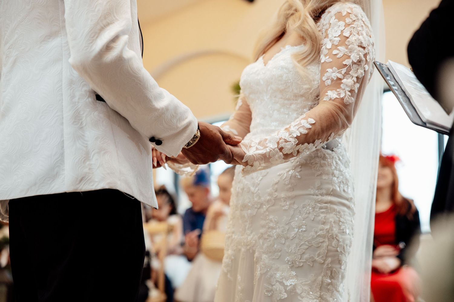 Bride and groom holding hands during wedding vows in a beautifully decorated ceremony venue.