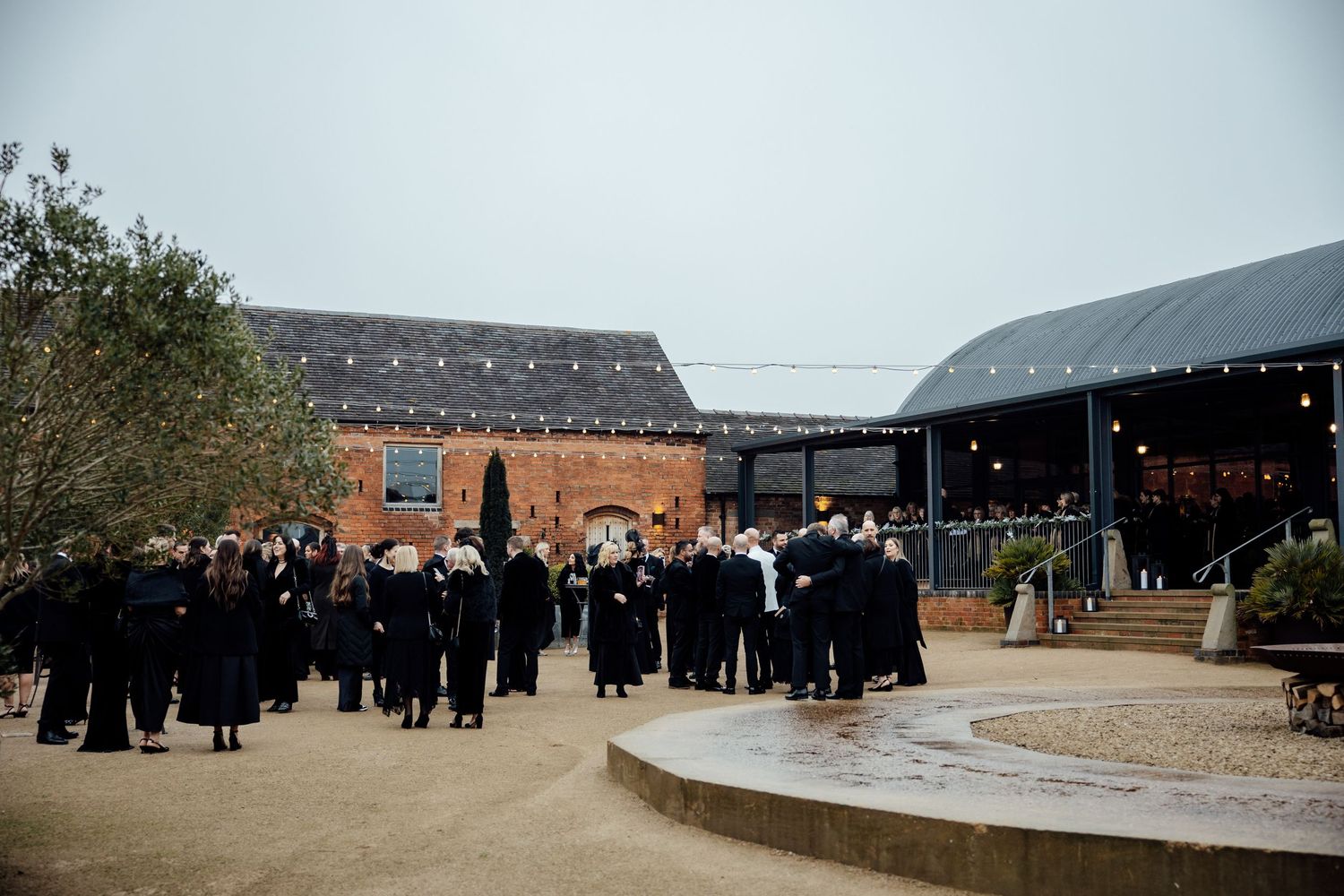 Large group of wedding guests gathered outside a rustic barn venue on an overcast day.