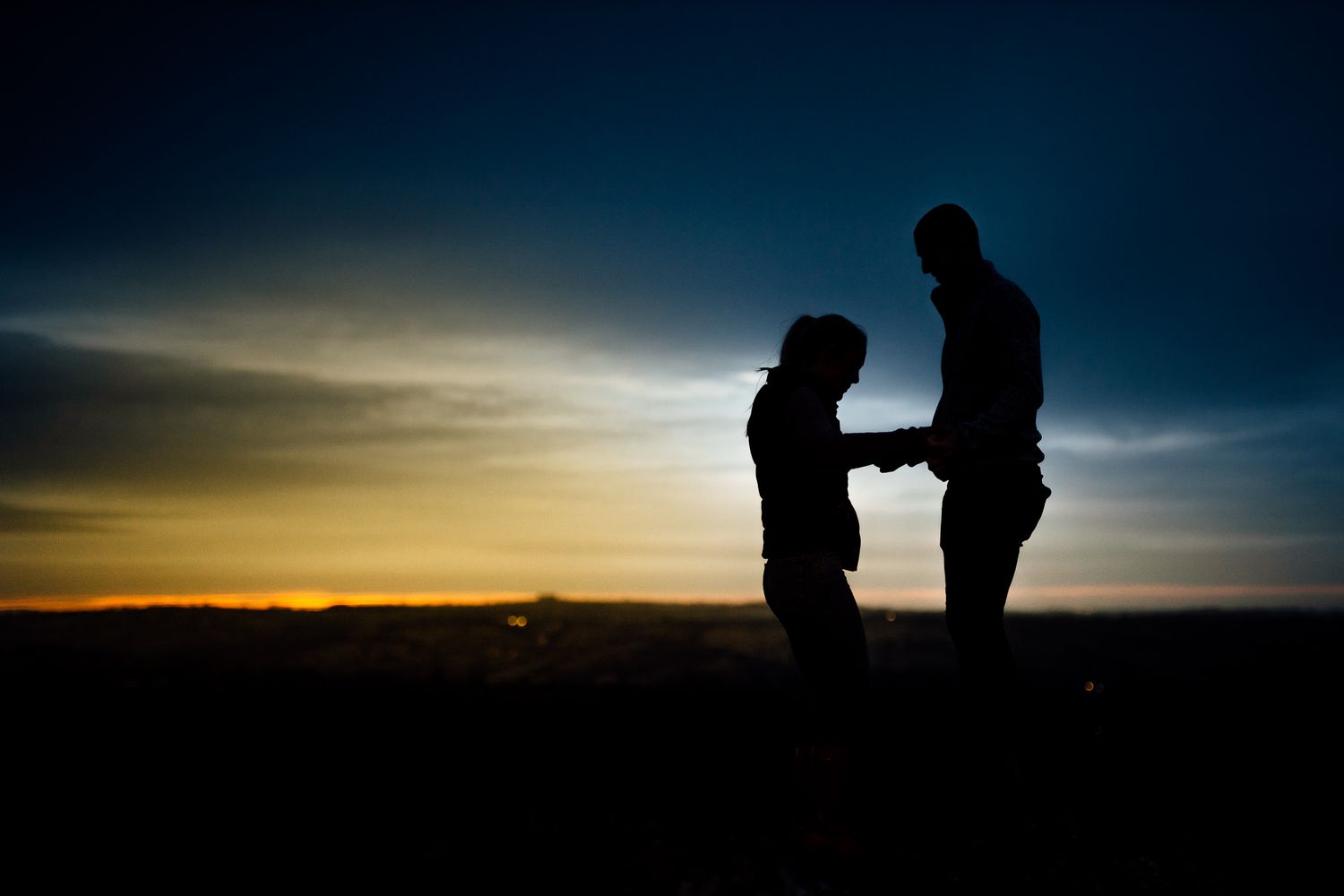 Silhouettes of a couple against a dramatic sunset sky in the mountains.