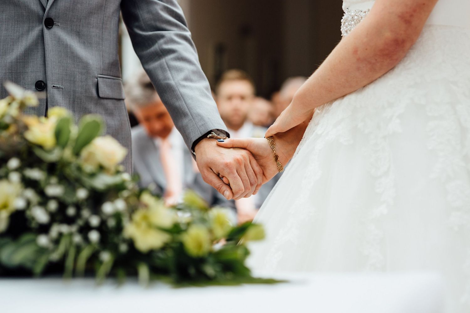 Close-up details of white wedding dress and formal attire during ceremony.
