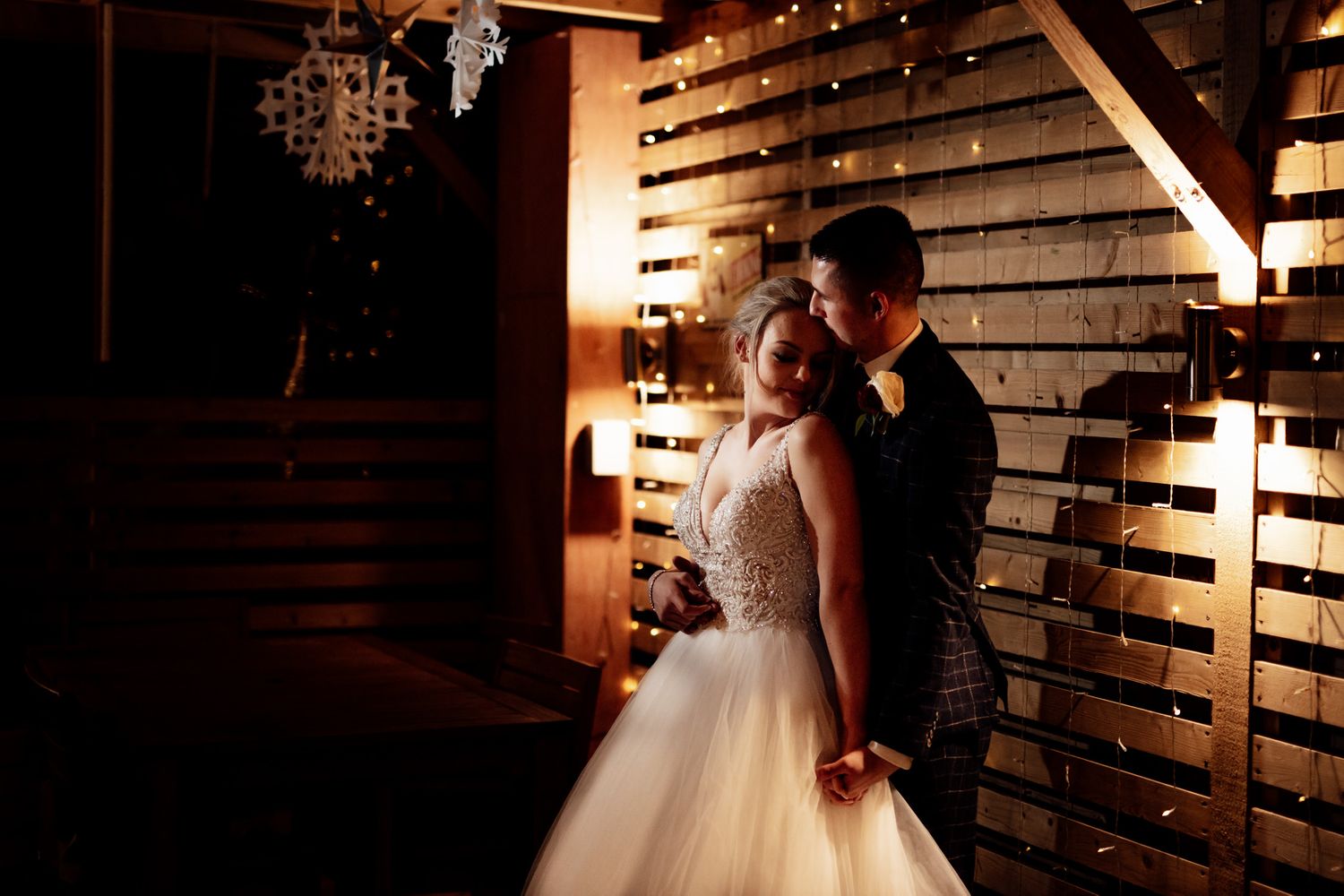 Wedding reception venue decorated with rustic wooden panels and romantic string lights.