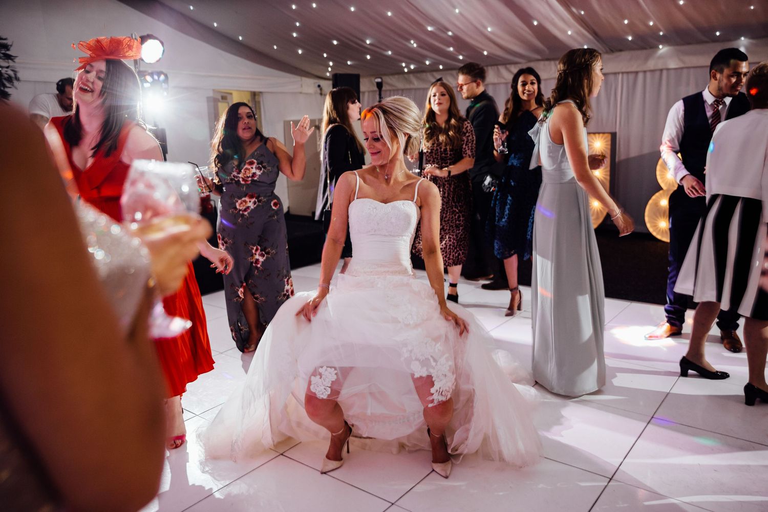 Wedding guests dancing and celebrating on an illuminated white dance floor at an indoor reception.