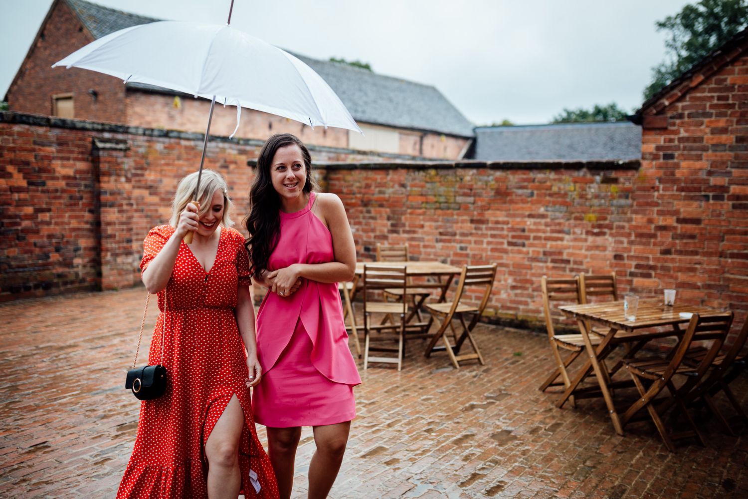 Bridesmaids in pink and coral dresses walking through a rustic brick courtyard.