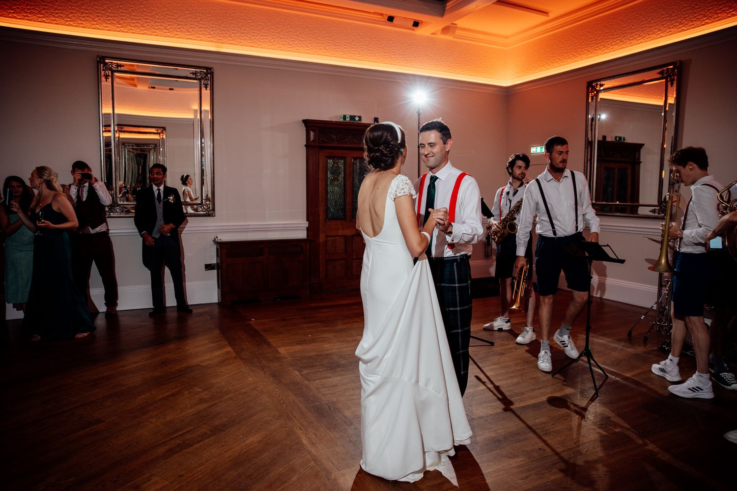 Wedding celebration on dance floor illuminated by warm orange ambient lighting.