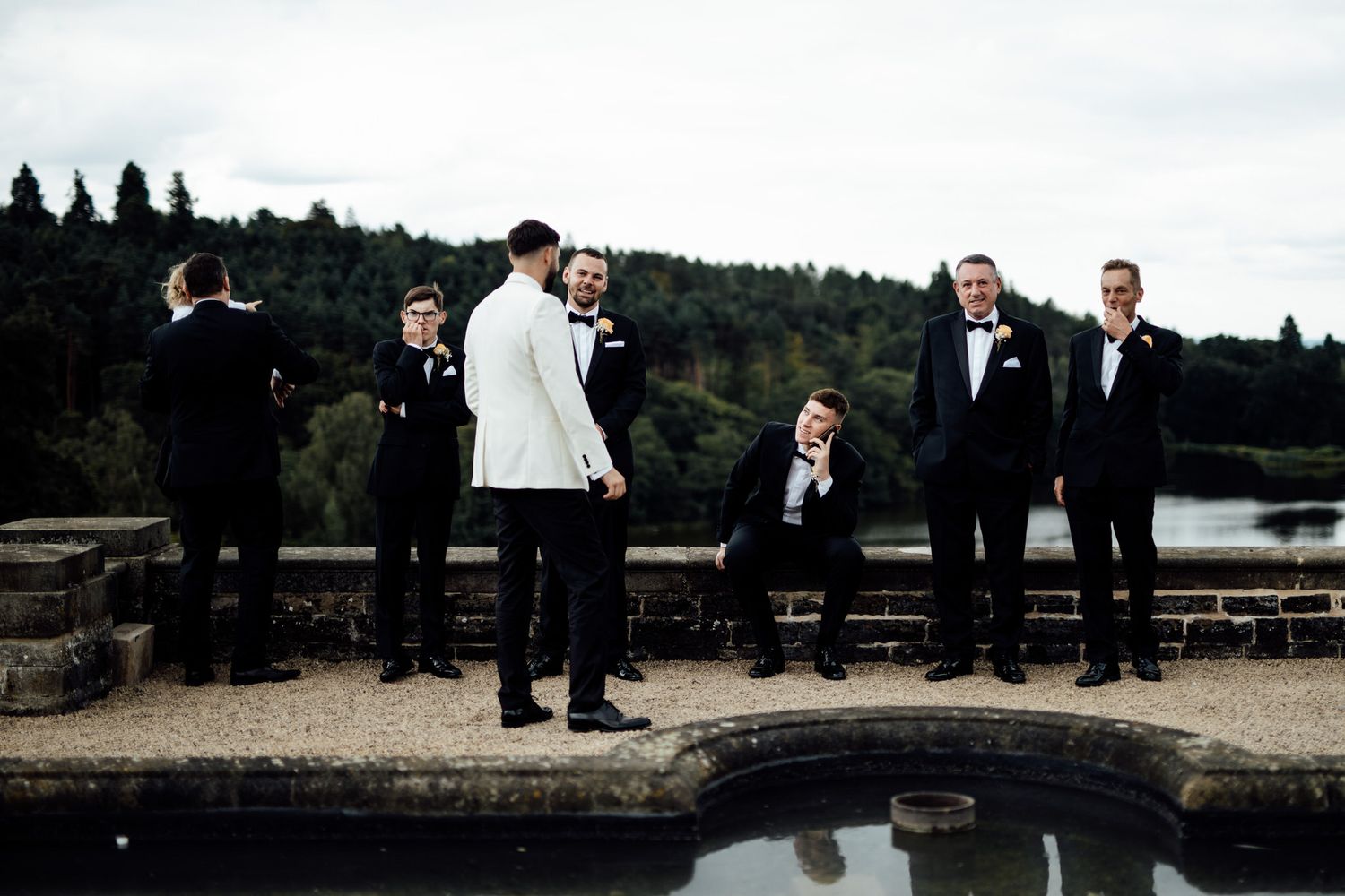 Wedding party and guests gather outdoors near a scenic lake at sunset.