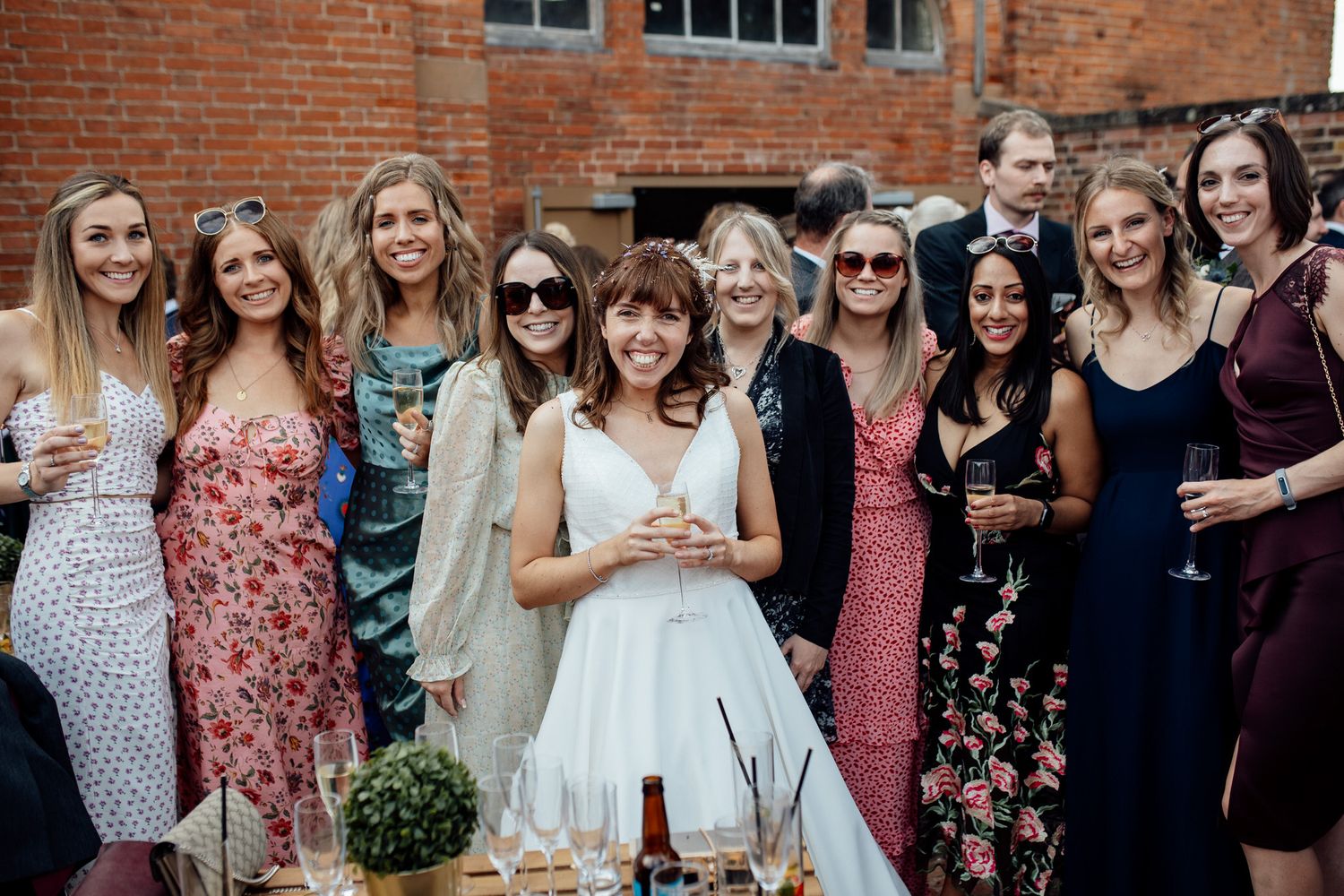 Group of wedding guests in floral dresses gathered for a casual outdoor photo.