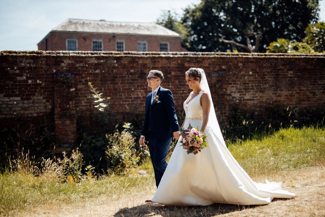 Wedding couple photographed along rustic brick wall in natural outdoor setting.