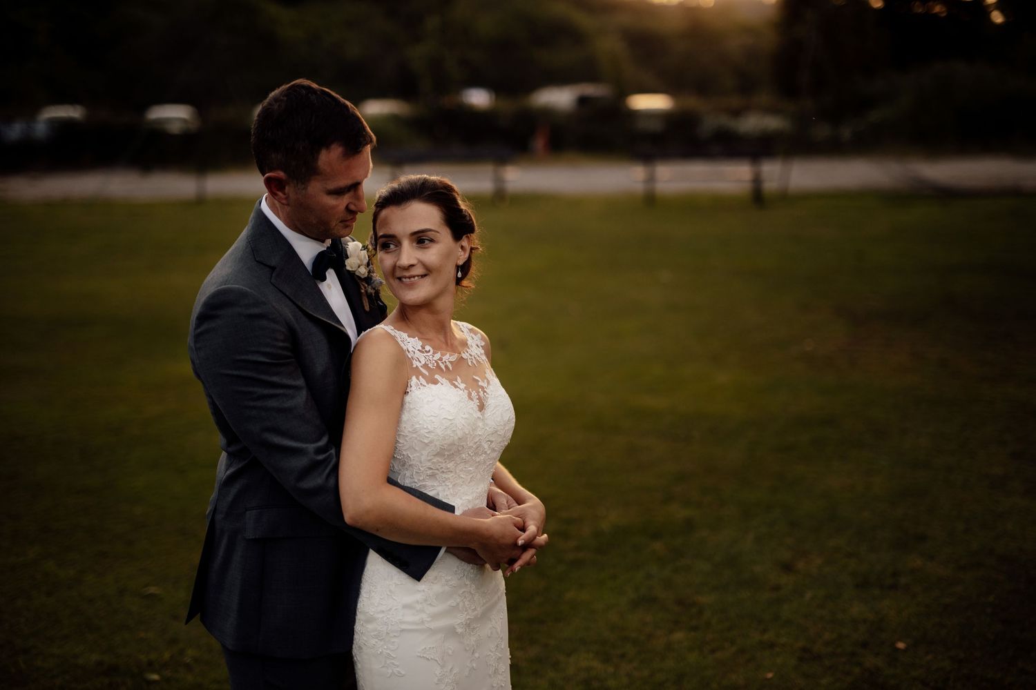 Couple shares an intimate moment at sunset in front of a rustic wooden fence.