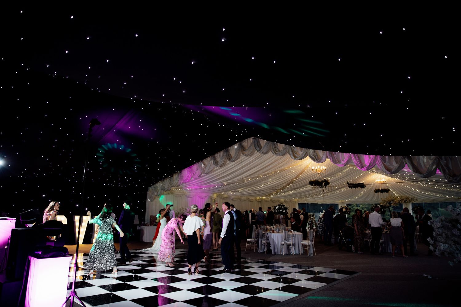Large wedding reception tent with black and white checkered dance floor and twinkling lights.