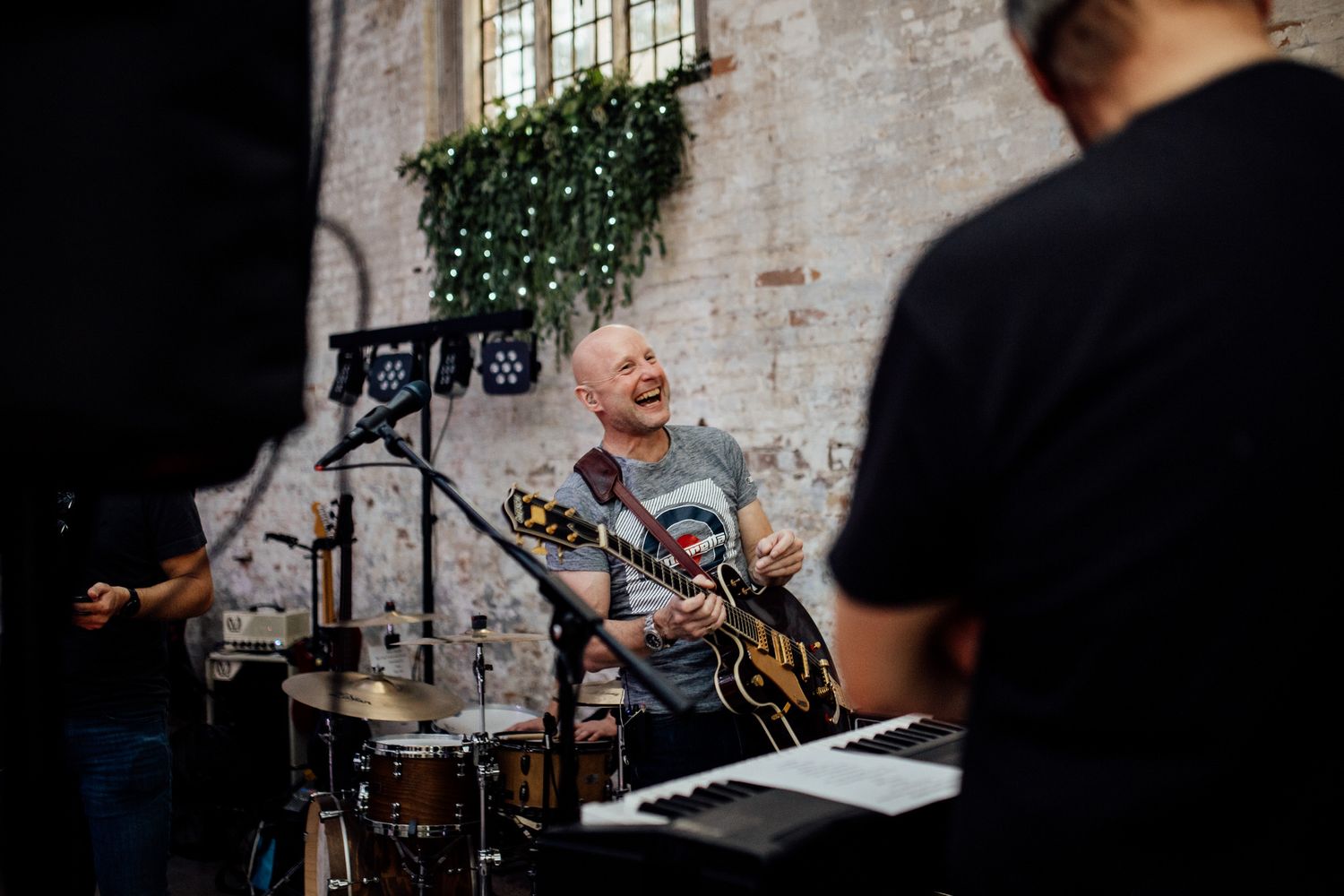 Musicians performing at indoor wedding reception with exposed brick walls and ambient lighting.