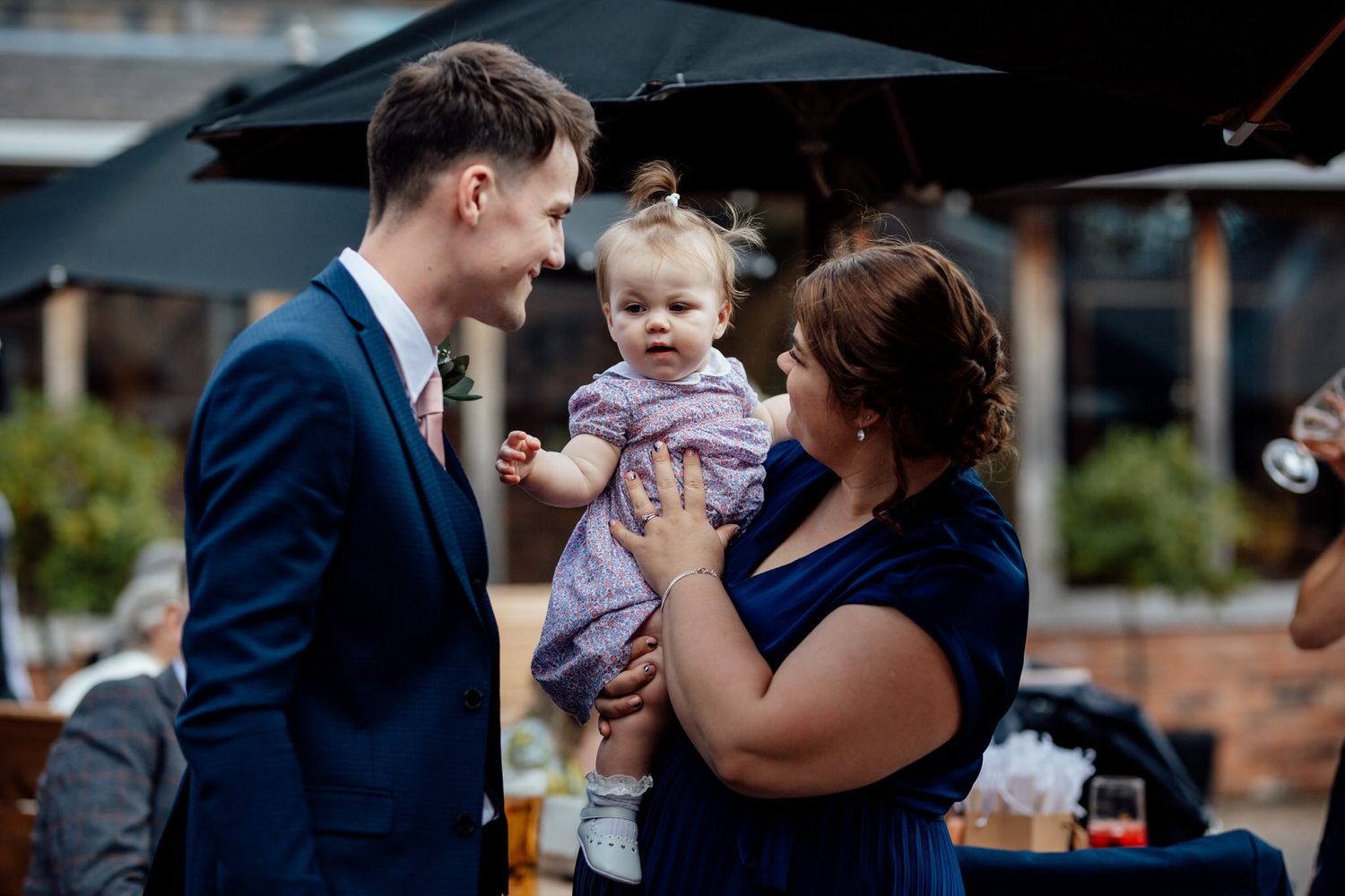 A couple shares an intimate moment with their baby under black umbrellas during an outdoor wedding ceremony.
