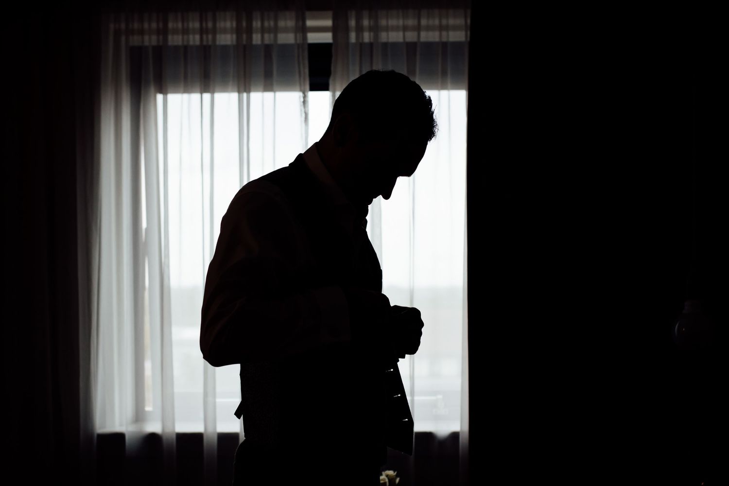 Silhouetted figures against bright window light creating dramatic wedding day portraits.
