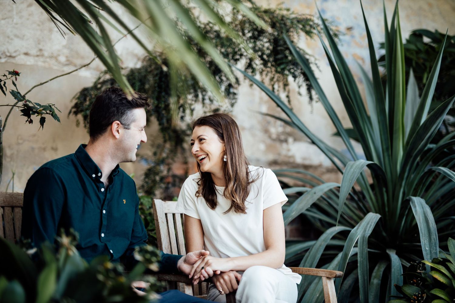 A romantic couple embraces in a garden setting with lush greenery and plants in the background.