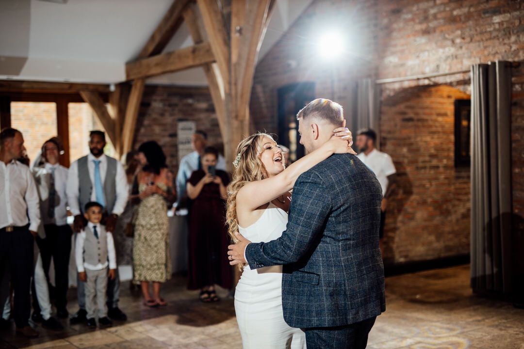First dance moment captured in rustic venue with exposed brick walls and wooden beams.