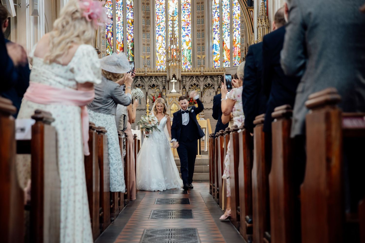 Church aisle view with wooden pews and stained glass windows during ceremony.