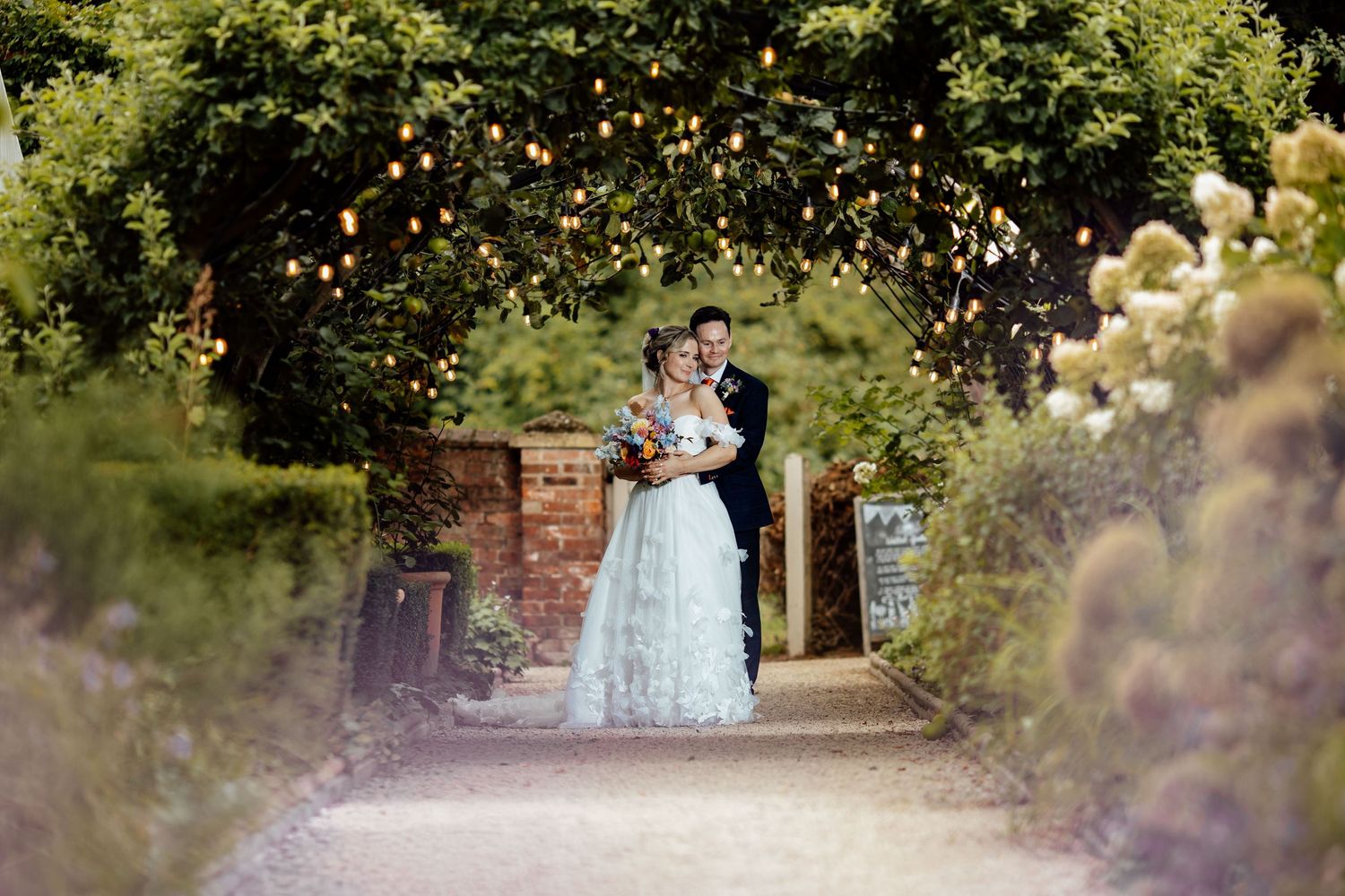 Dreamy garden wedding scene with string lights twinkling through lush green foliage.