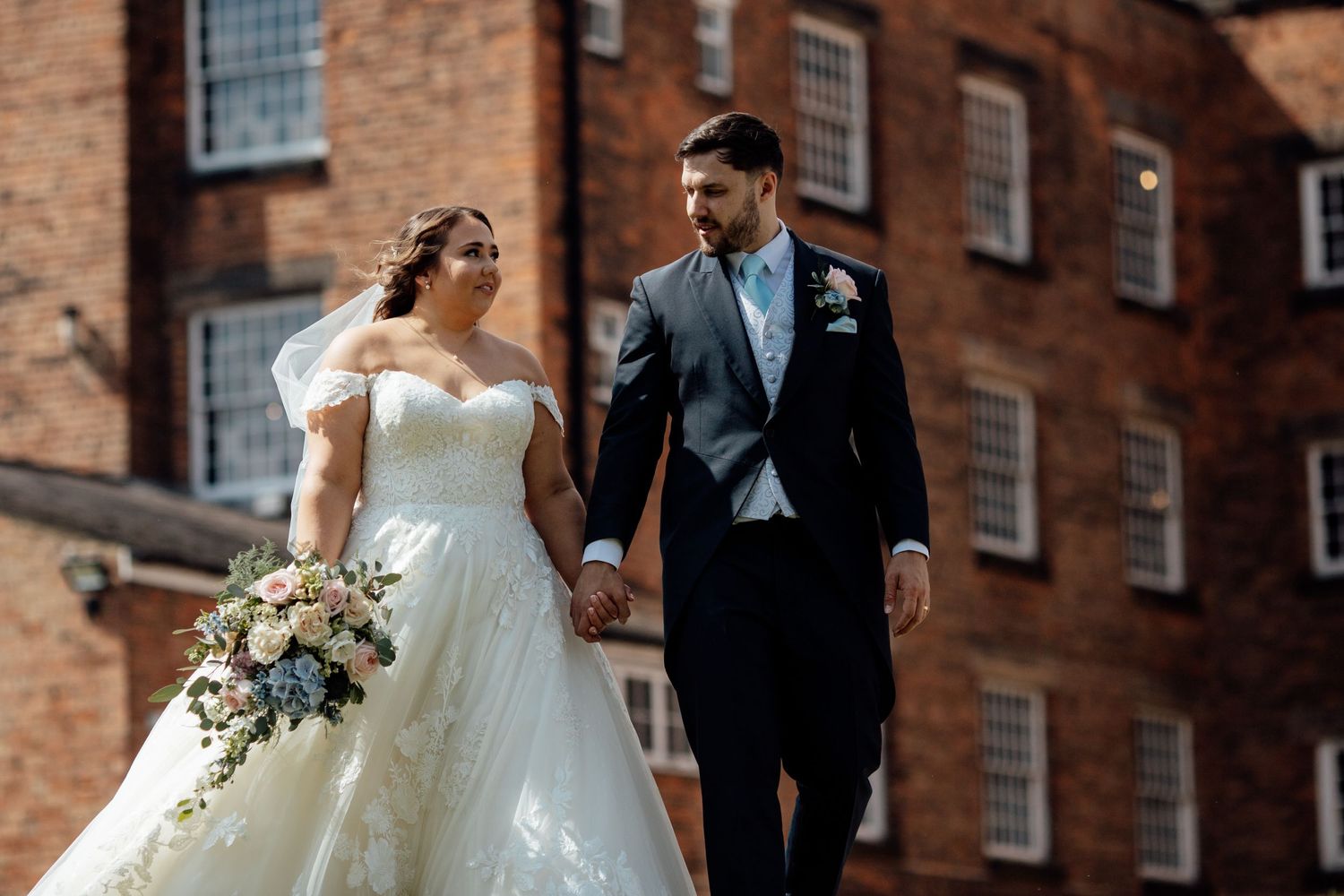 Bride and groom walking together outside historic brick building.