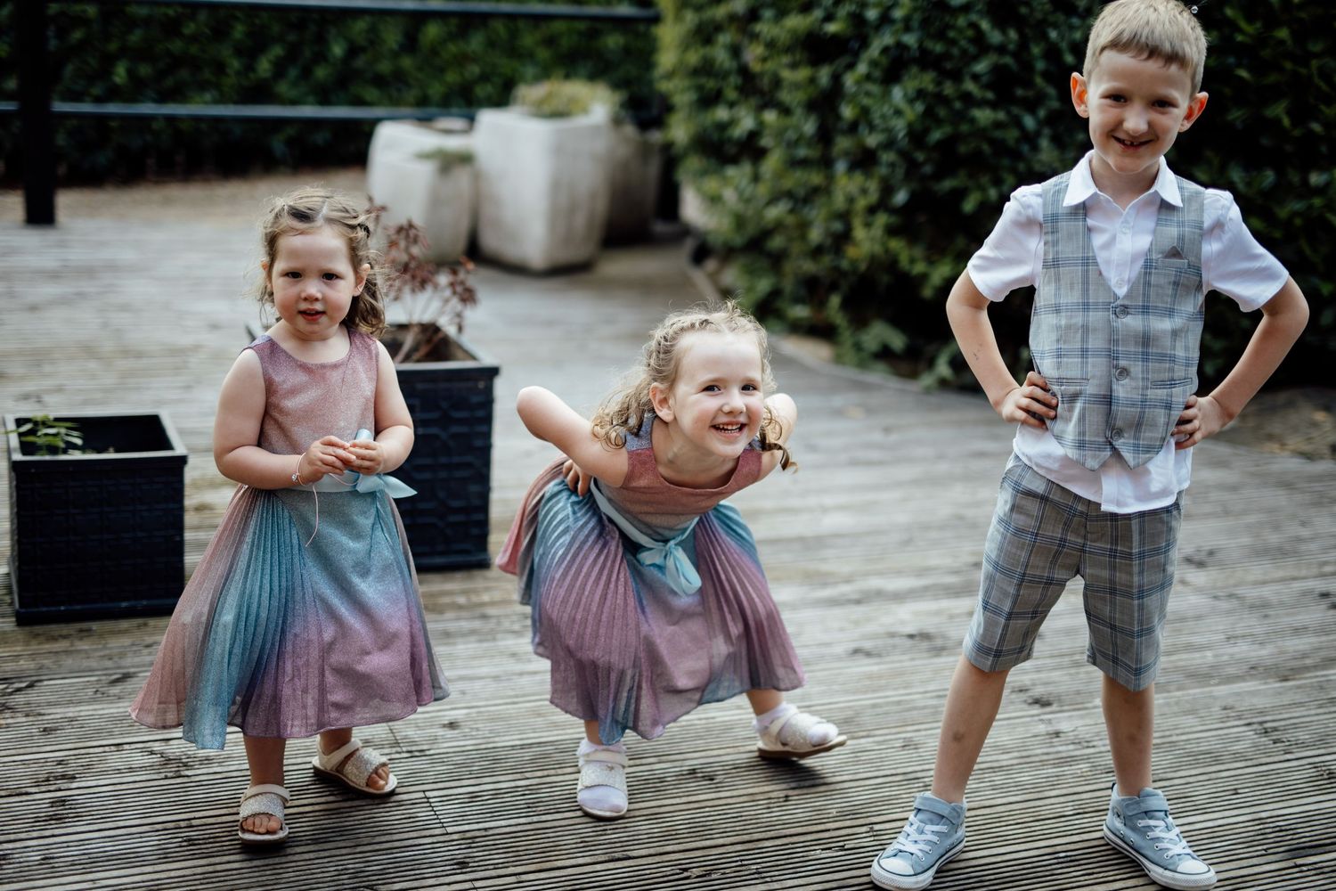 Children in formal attire play together on cobblestone ground during wedding festivities.