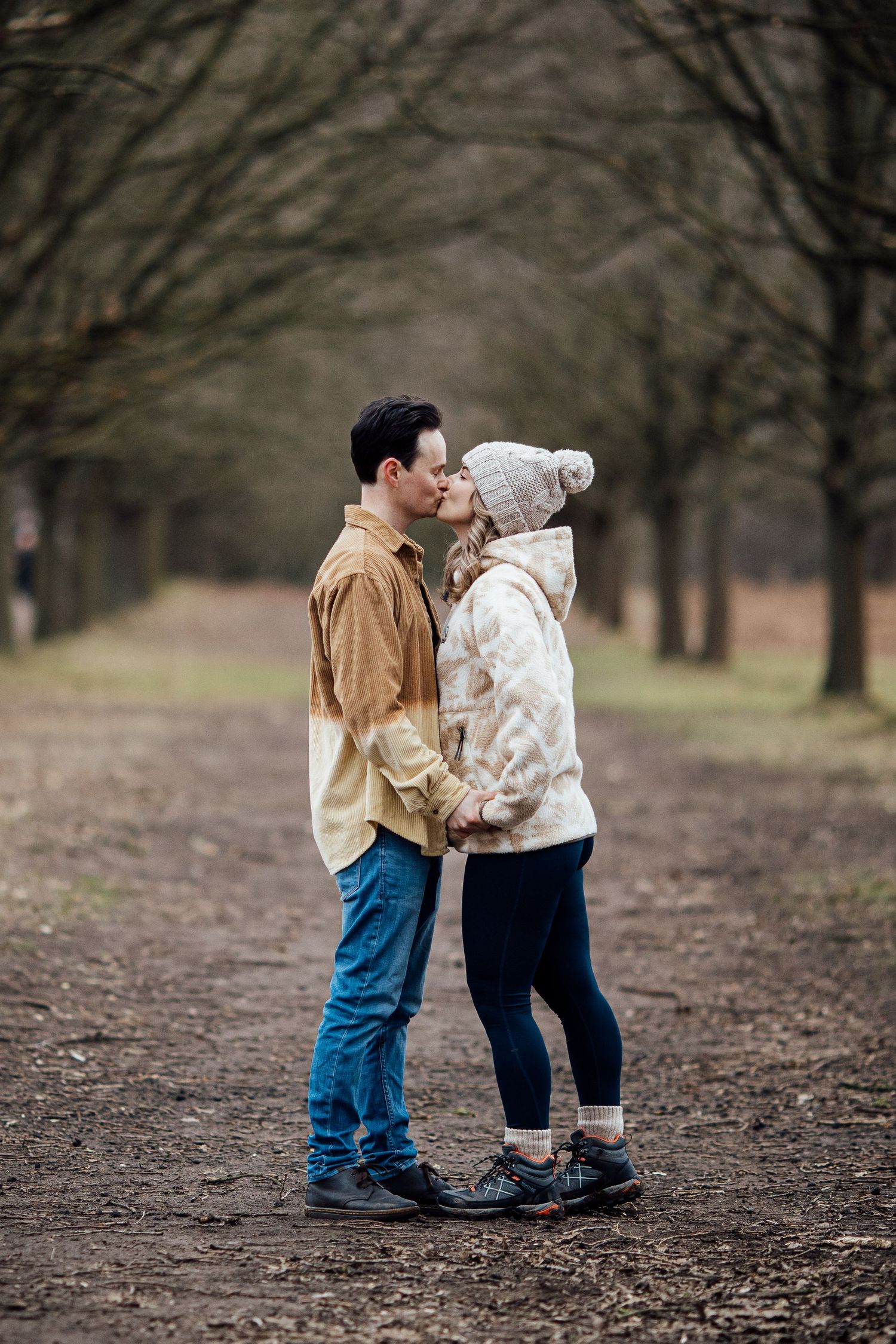A romantic winter photoshoot in a wooded park with bare trees in the background.