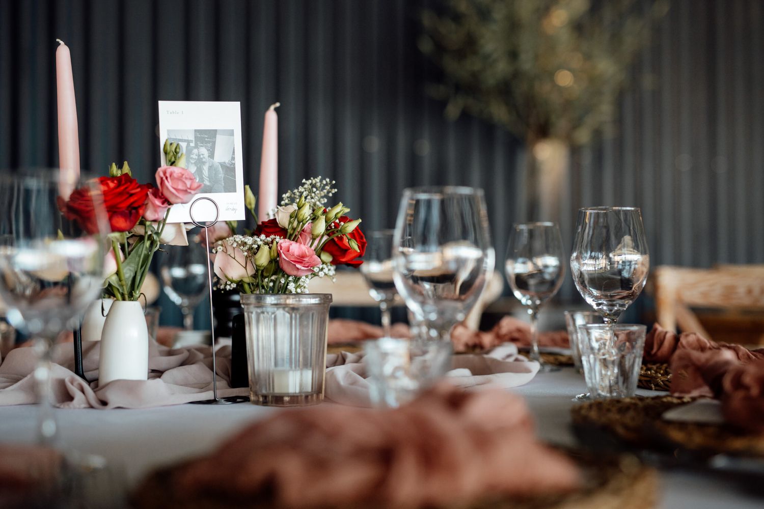 Elegant table settings with red flowers and glassware at wedding reception.