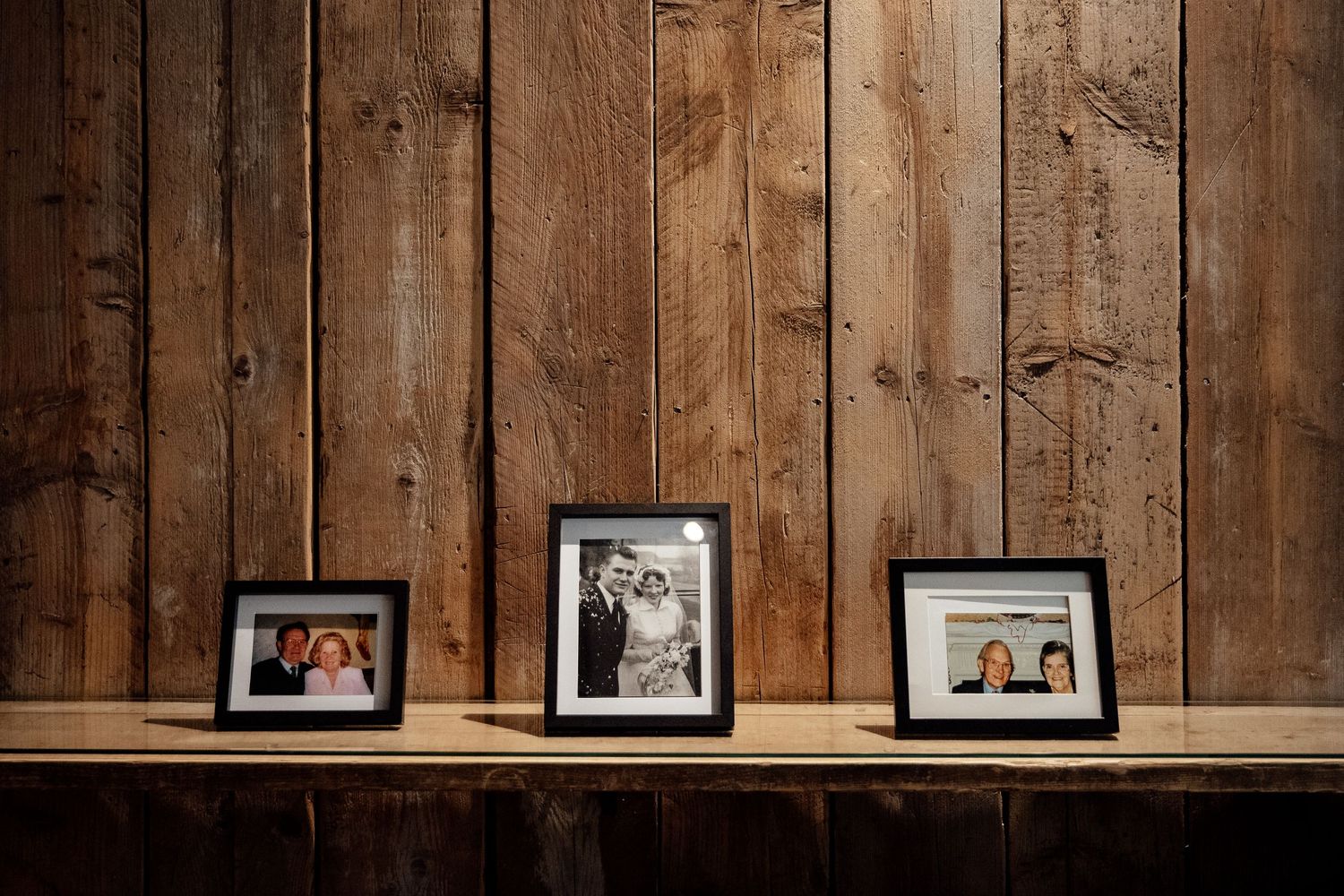 Rustic wooden wall with framed photographs displayed on a shelf creates vintage wedding decor.